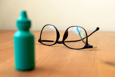 Eye glasses on a wooden table with a plastic container blurred in the foreground 