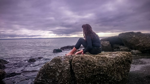 Man sitting on rock by sea against sky