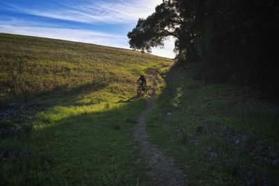 Person bicycling on dirt road against sky