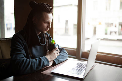 Hipster man using laptop while having drink in cafe