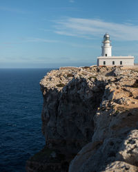 Lighthouse on cliff by sea against sky