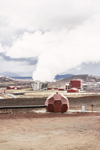 Geothermal station with industrial buildings with smoke located in volcanic area of iceland against cloudy sky and mountains