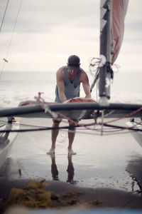 Man standing by windsurfing board at beach