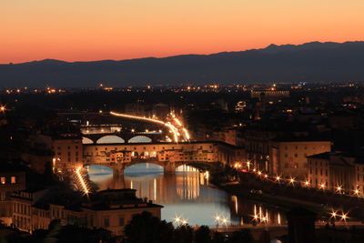 Illuminated bridge over river in city at sunset