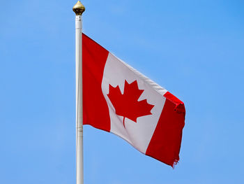 Low angle view of canadian flag waving against clear blue sky