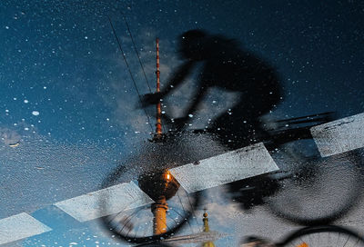 Reflection of woman riding bicycle and fernsehturm on puddle at street