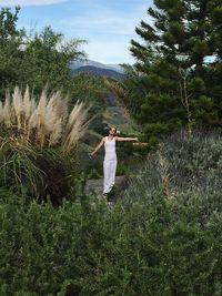 Full length of happy woman standing with arms outstretched amidst plants