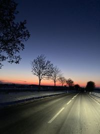 Silhouette trees by road against sky during sunset
