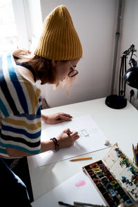 Side view of female artist in fancy wear sitting at table in studio and browsing mobile phone during work