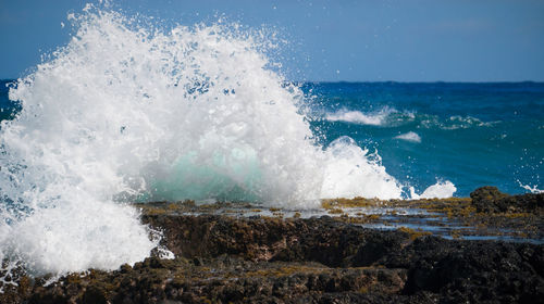 Waves splashing on rocks at shore against sky