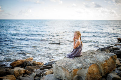 Woman sitting on rock by sea against sky