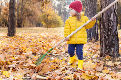 Cute kid standing with broom by trees during autumn