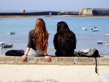 Friends sitting on retaining wall in front of sea