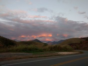 Road leading towards mountains against cloudy sky