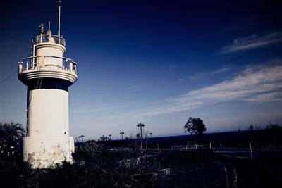 Lighthouse by street light against sky