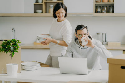 Woman looking at laptop being used by man on table at home