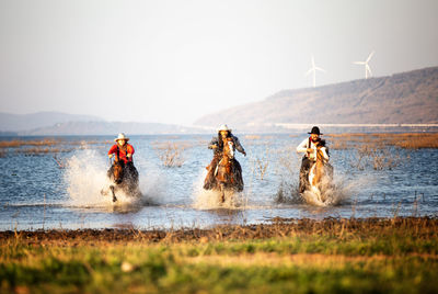 People riding horses in lake against sky