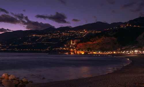 Illuminated beach by sea against sky at night