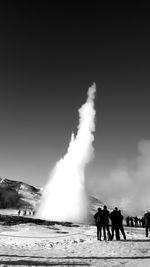 People looking at strokkur geyser erupting against clear sky