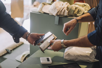 Cropped hands of male customer and clerk doing mobile payment at checkout in clothing store