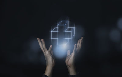 Close-up of hand holding illuminated lighting equipment against black background