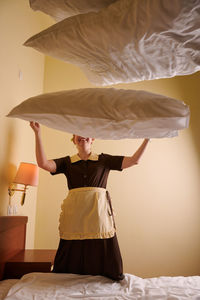 Rear view of woman with umbrella standing on bed at home