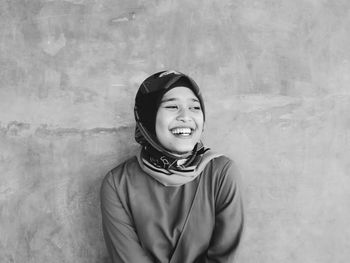 Portrait of smiling young woman standing against wall