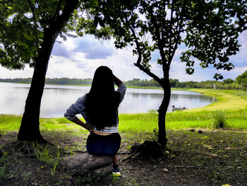 Rear view of woman standing by lake against sky