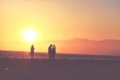 Silhouette men on beach against clear sky during sunset