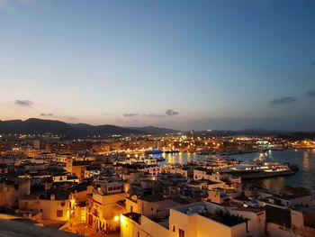 High angle view of illuminated city by sea against sky