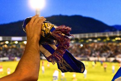 Close-up of hand holding illuminated soccer scarf against sky