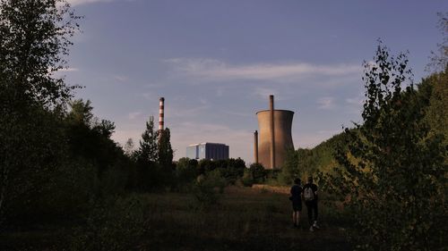 Men standing by factory against sky