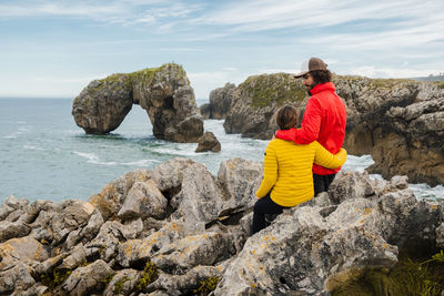 Rear view of women on rock formation by sea against sky