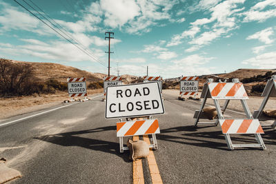 Warning signs on country road against cloudy sky