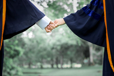 Midsection of couple in graduation gown giving pinky promise