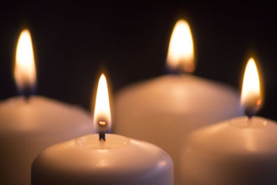 Close-up of illuminated lit candles against black background