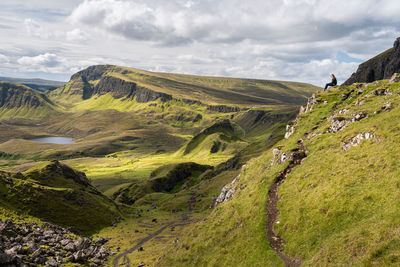 Girl sitting on rock and looking at view of rocky outcrop in the quiraing, isle of skye, scotland