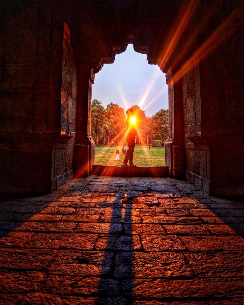 SUNLIGHT STREAMING THROUGH SILHOUETTE MAN STANDING AGAINST BUILDINGS