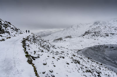 Distant view of people walking on covered mountain road against sky