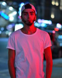 Young man looking away while standing in illuminated city at night