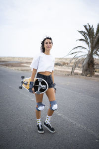 Smiling young woman with skateboard walking on road