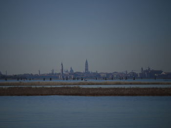 View of buildings by river against clear sky