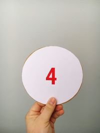 Cropped hand of person holding number on cardboard against gray background