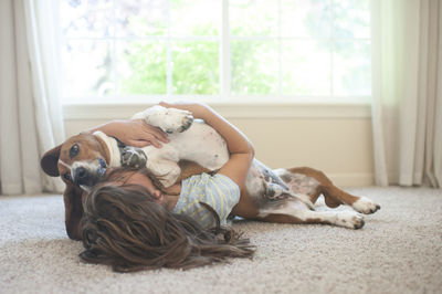 Young girl laying with her basset hound dog on the floor at home