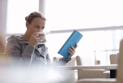 Woman drinking coffee while holding digital tablet