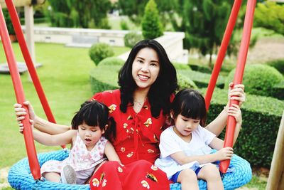 Portrait of mother with cute daughters sitting on swing in park