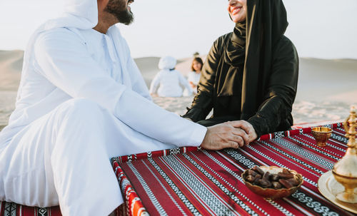 Midsection of arabian couple sitting at desert