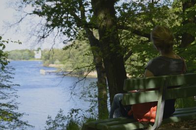 Rear view of man sitting by lake against trees