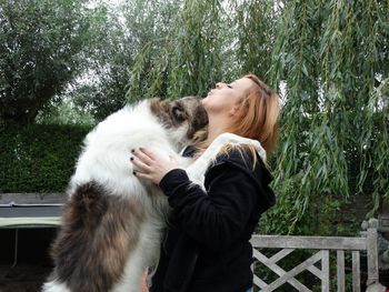 Side view of woman standing with dog against trees