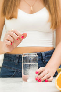 A woman throws a white round pill into a glass of water. pain reliever,